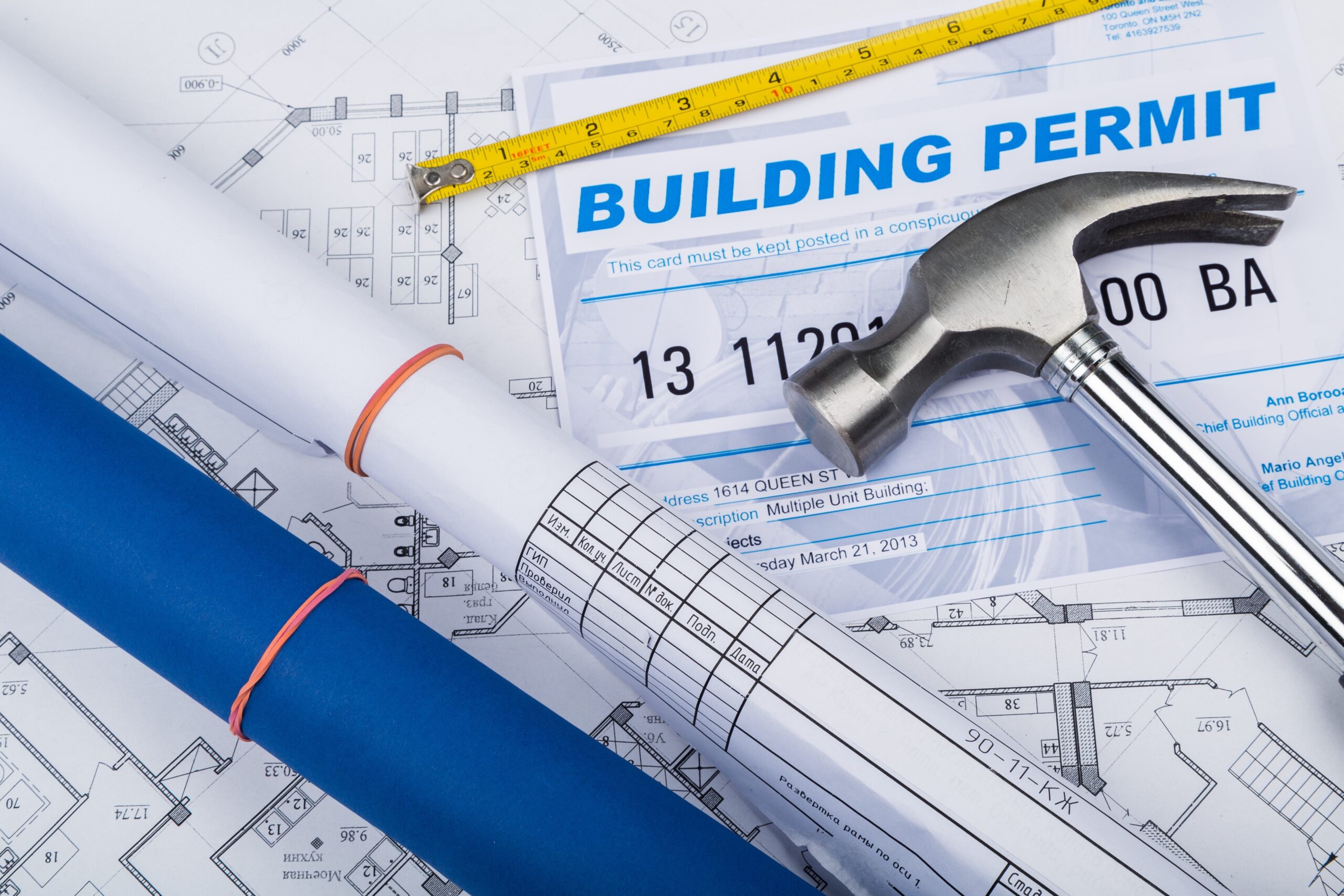 Pile of building permits, design documents, and floor plans with a hammer and tape measure, representing construction planning and project management