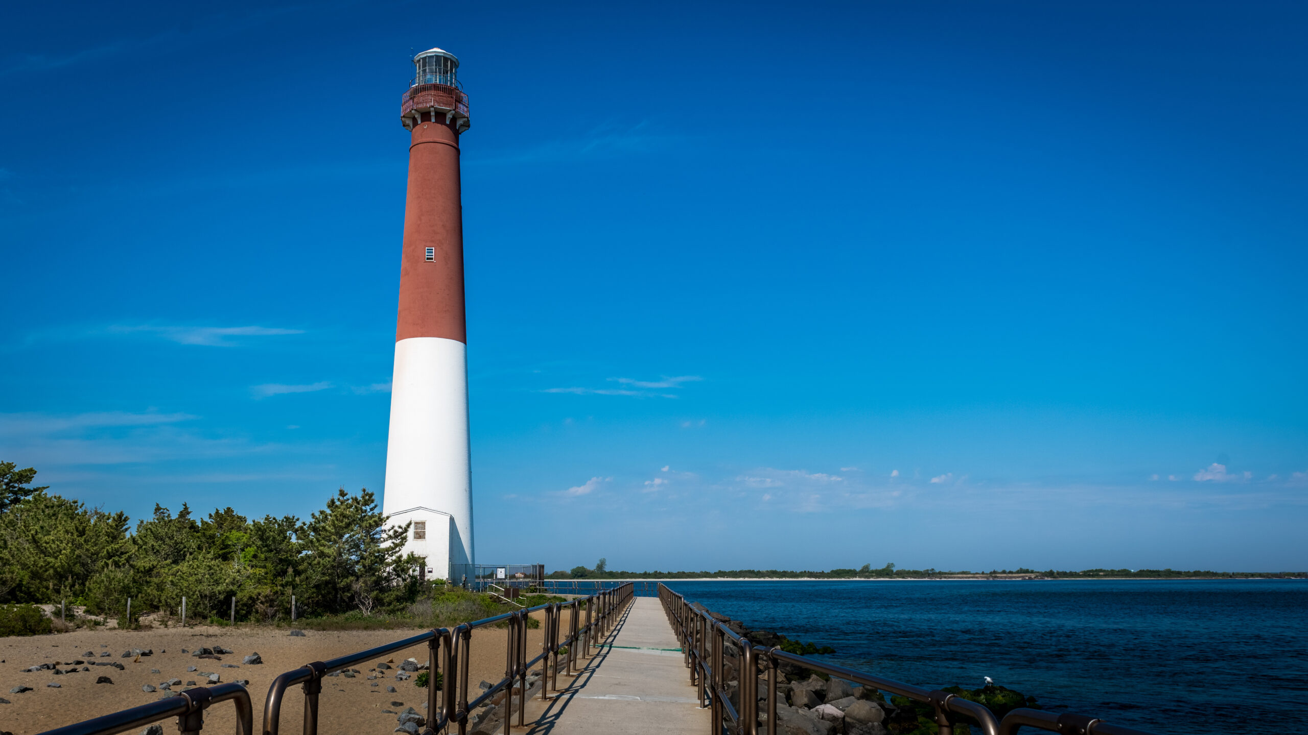Pathway along the ocean leading to a lighthouse on a sandy beach, showcasing coastal scenery and maritime landmarks