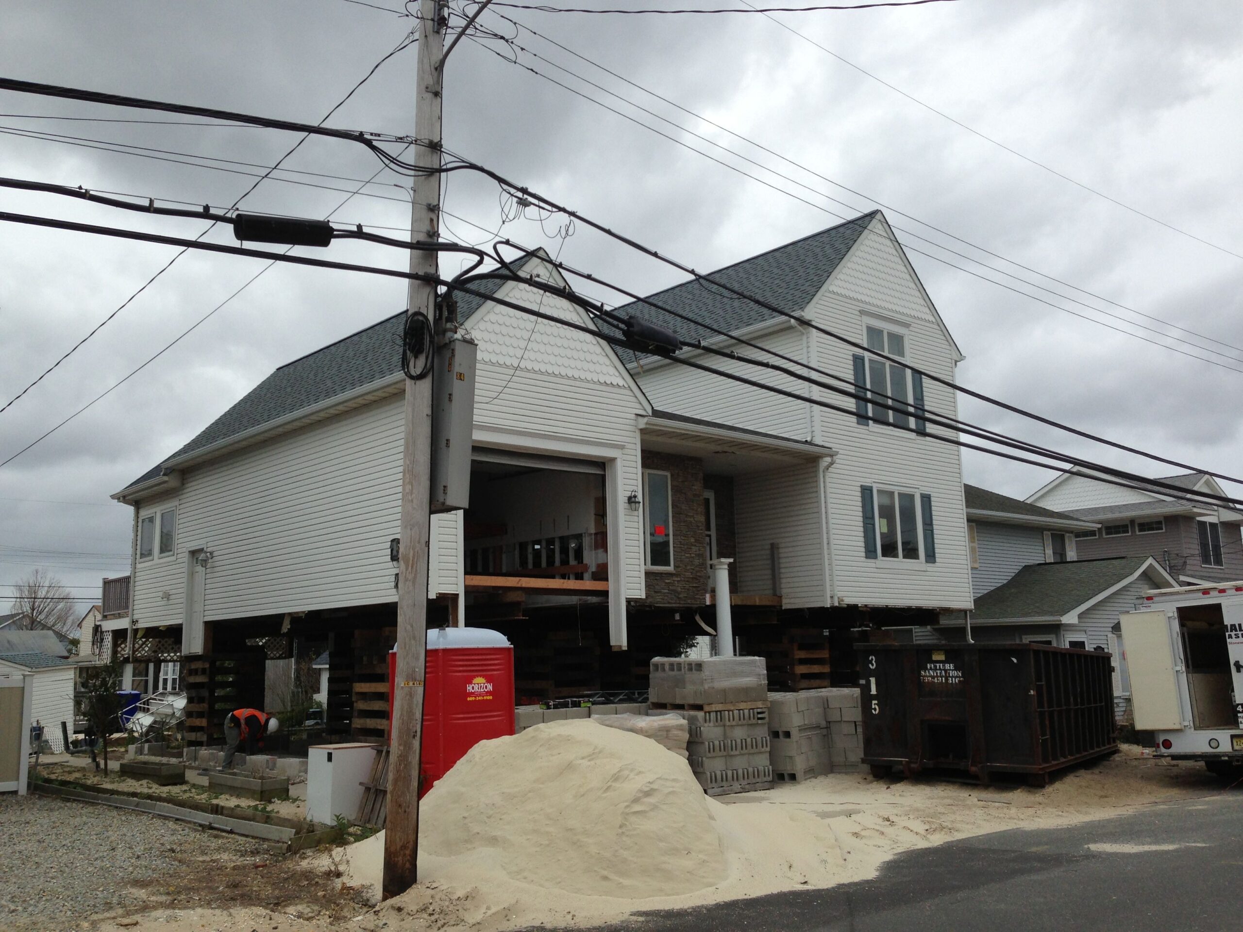 House under construction with a pile of sand, dumpster, and building materials, showcasing residential building progress and construction site setup